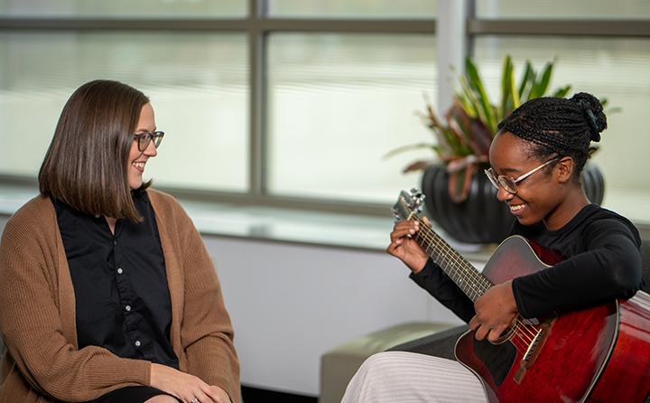 music therapy student playing guitar next to professor